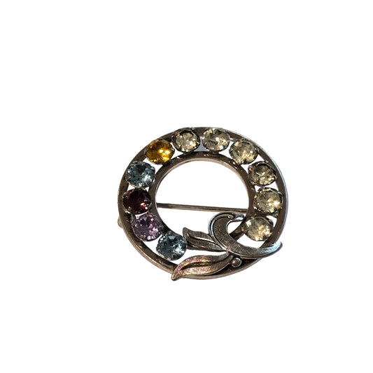 Circular brooch with multicolored gemstones on a white background
