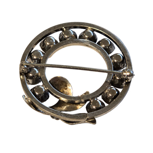 Silver circular brooch with small stones on a white background