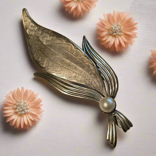 Silver leaf-shaped brooch with a pearl on a light gray background