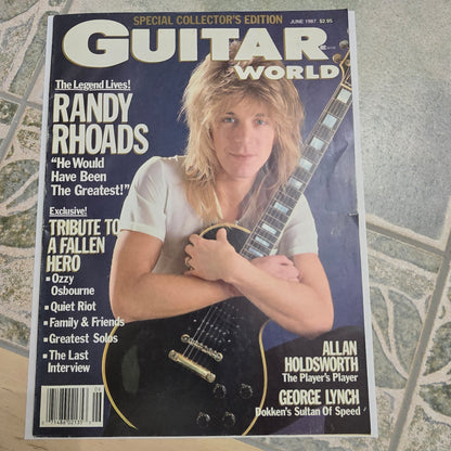 Magazine cover featuring a woman holding a guitar with text about Randy Rhoads on a textured surface.
