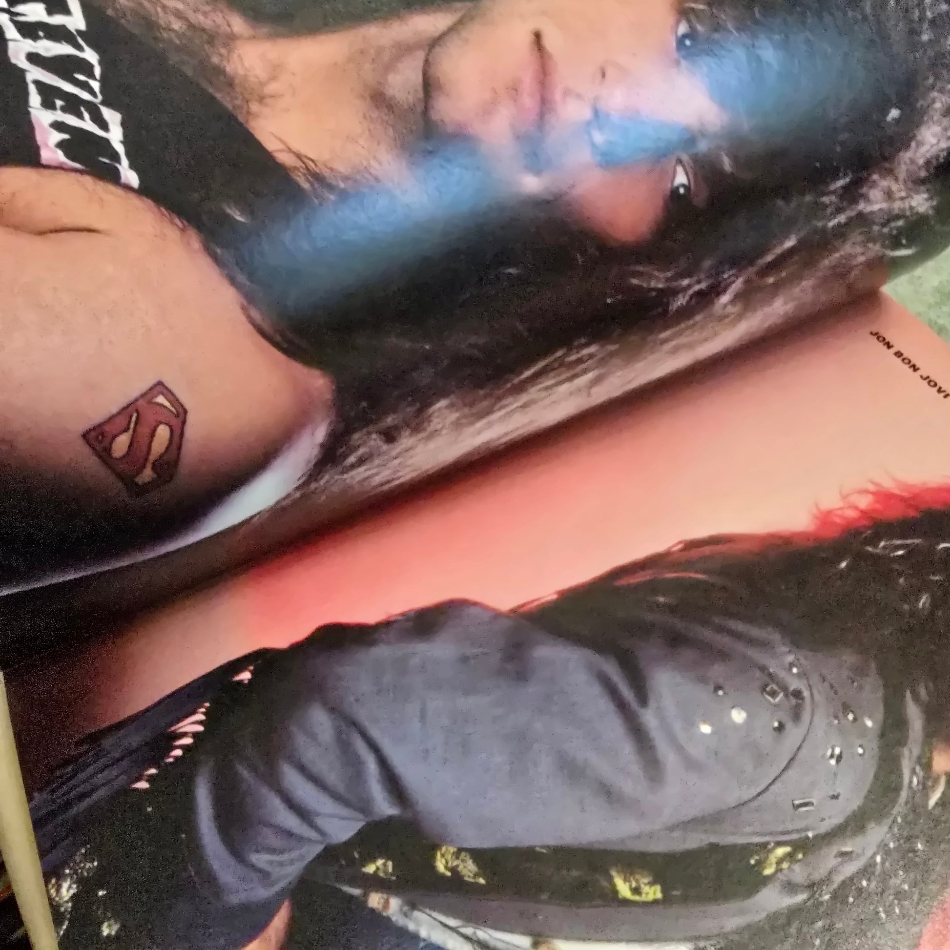 Person with a Superman tattoo on their arm, leaning against a book.
